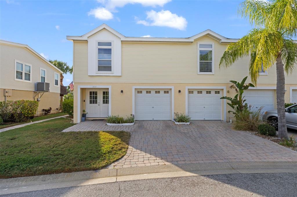 A two-story townhouse with yellow siding, a paver driveway, and two garage doors — 7641 SAILWINDS PASS, PORT RICHEY, FL