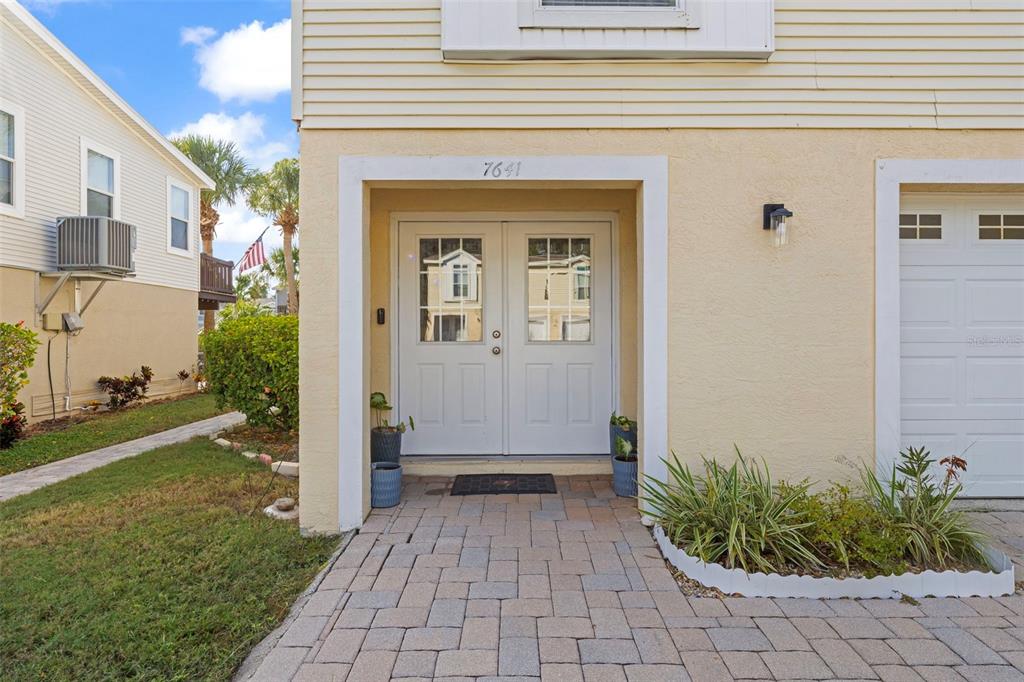A paved walkway leads to the double front doors of a tan house with a garage — 7641 SAILWINDS PASS, PORT RICHEY, FL