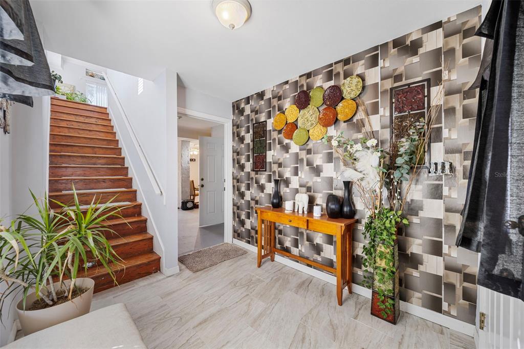 An entryway features a wooden staircase, patterned wallpaper, a console table, and tile flooring — 7641 SAILWINDS PASS, PORT RICHEY, FL
