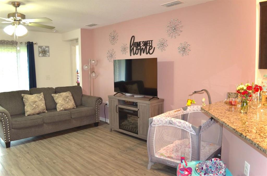 A living room features a grey sofa, a television on a console, and a playpen — 1639 SWAN LAKE CIRCLE, DUNDEE, FL