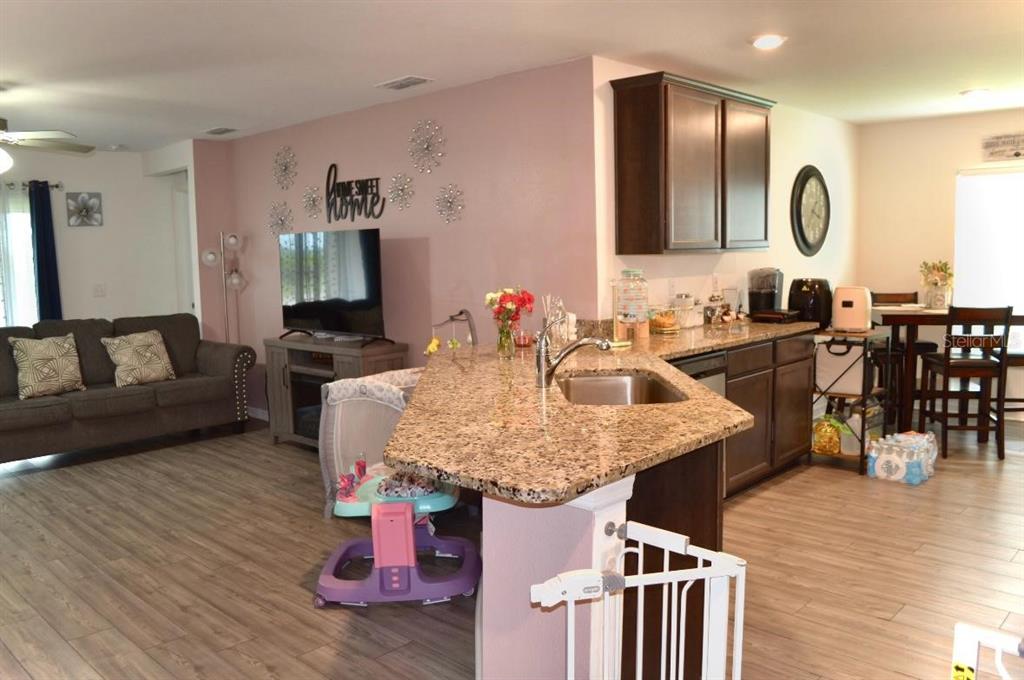 An open-concept kitchen with granite countertops overlooks a living room with a gray sofa — 1639 SWAN LAKE CIRCLE, DUNDEE, FL