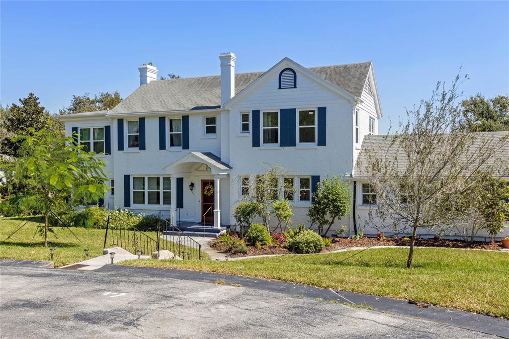 A two-story white brick house features blue shutters, a red front door, and a shingled roof — 694 LAKE OTIS DRIVE SE, WINTER HAVEN, FL