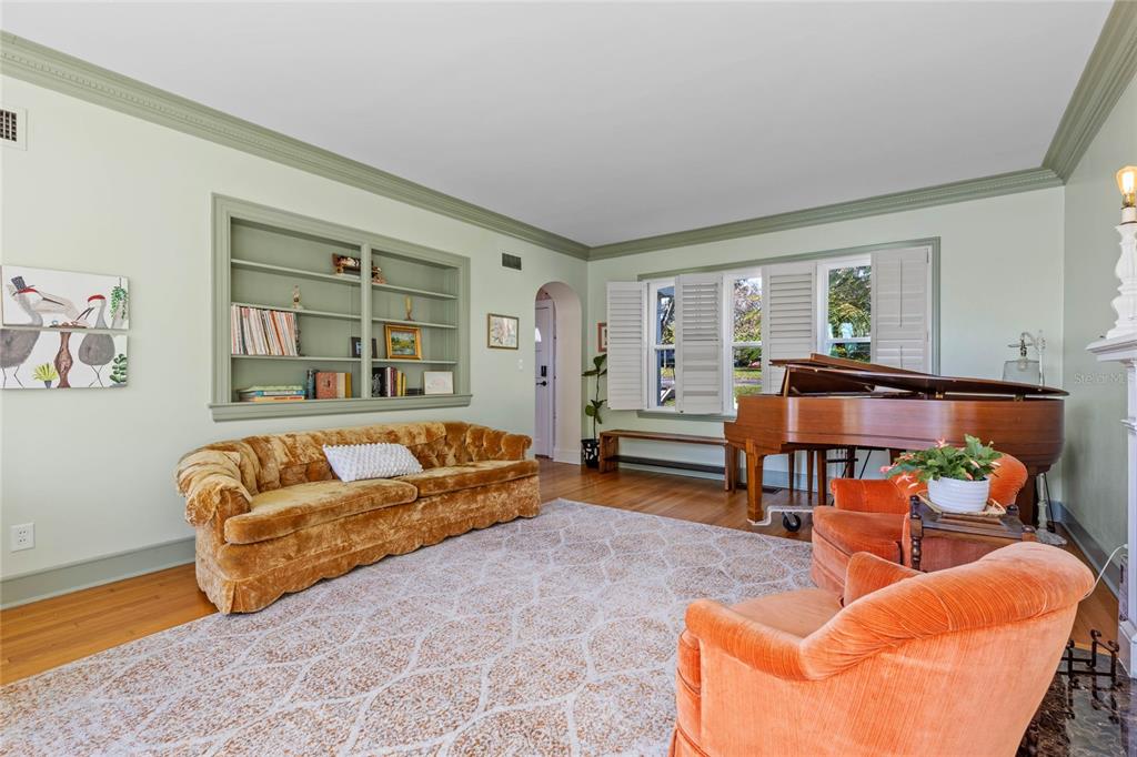 A living room features a velvet sofa, two orange armchairs, a grand piano, and built-in shelving — 694 LAKE OTIS DRIVE SE, WINTER HAVEN, FL