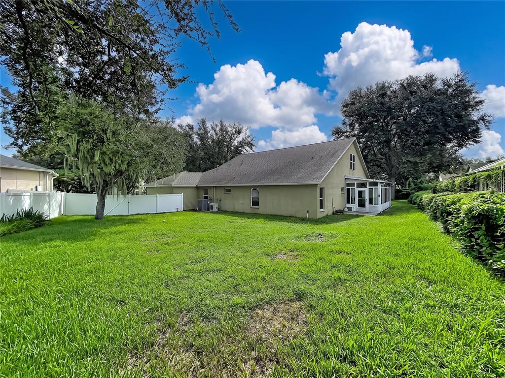 A view of a house exterior with a grassy backyard, white fence, and screened porch — 1124 SPLIT SILK STREET, VALRICO, FL