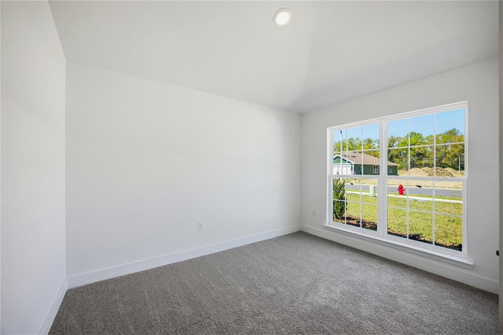 An empty bedroom with white walls, gray carpet, and a large window overlooking a street — 13855 NW 150TH CIRCLE, ALACHUA, FL
