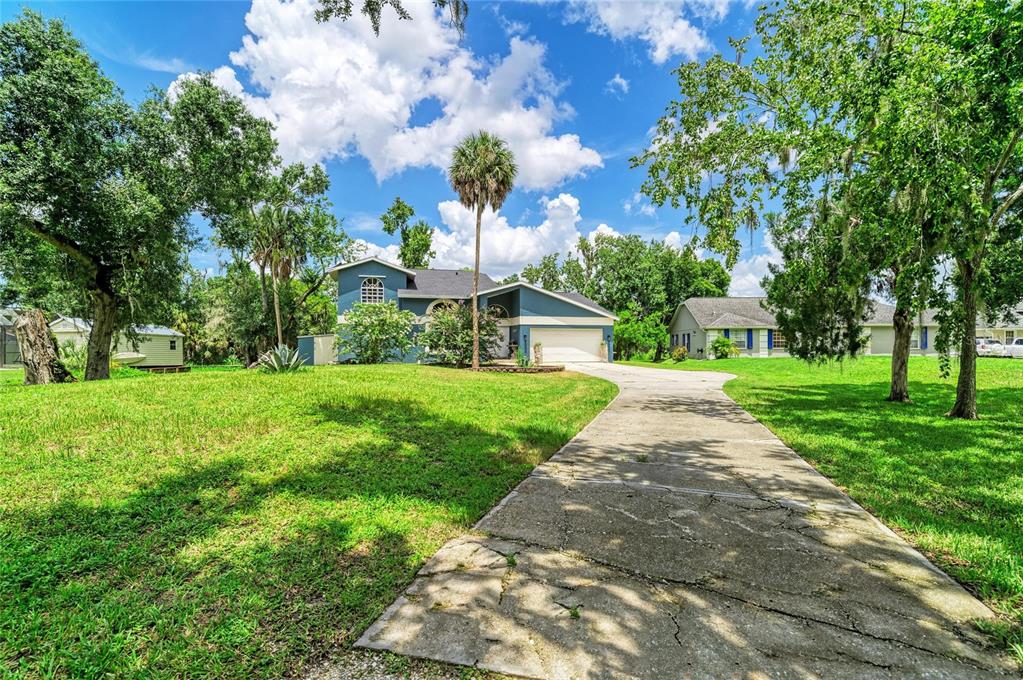 A blue two-story house with a concrete driveway sits on a large, grassy, tree-filled lot — 6519 28TH AVENUE E, BRADENTON, FL