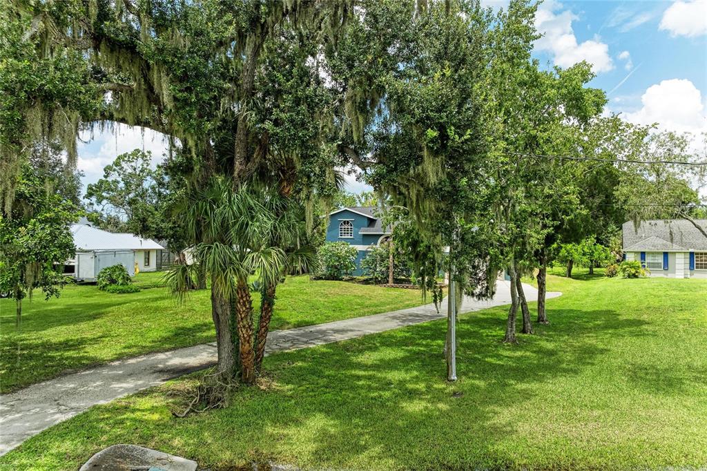 A long driveway leads to a blue house surrounded by large trees and green lawns — 6519 28TH AVENUE E, BRADENTON, FL