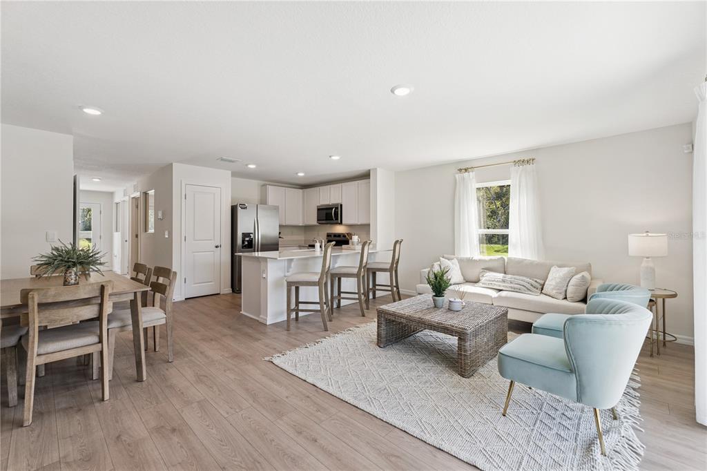 An open-concept living room and kitchen featuring light wood flooring and white cabinetry — 1665 GREAT OSPREY WAY, NEW SMYRNA BEACH, FL
