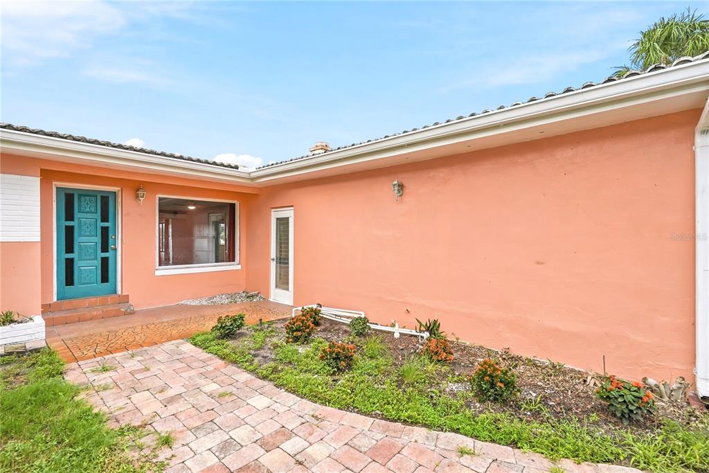 A peach-colored house exterior features a teal front door, a window, and a brick walkway — 3860 BELLE VISTA E, ST PETE BEACH, FL