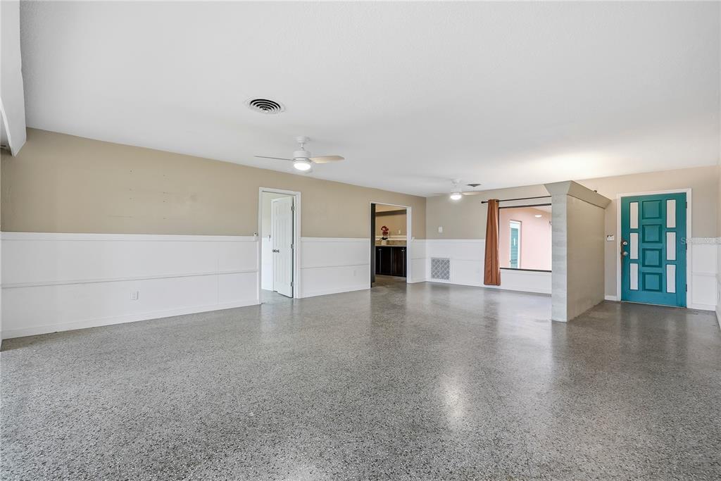 A spacious room with speckled epoxy flooring, white wainscoting, two ceiling fans, and a teal door — 3860 BELLE VISTA E, ST PETE BEACH, FL