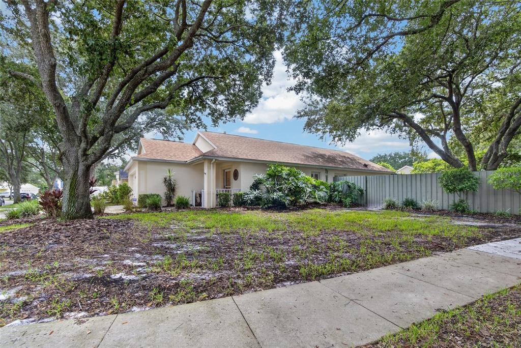 A single-story house with a beige exterior sits behind a lawn shaded by large trees — 5848 MEADOWPARK PLACE, LITHIA, FL