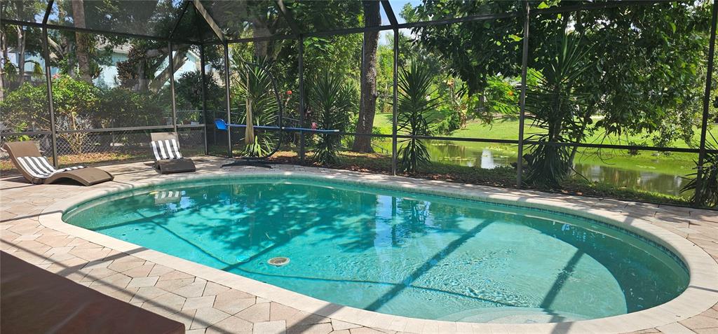 An oval swimming pool with a paved deck is enclosed by a screened lanai overlooking water — 4907 82ND PLACE E, SARASOTA, FL