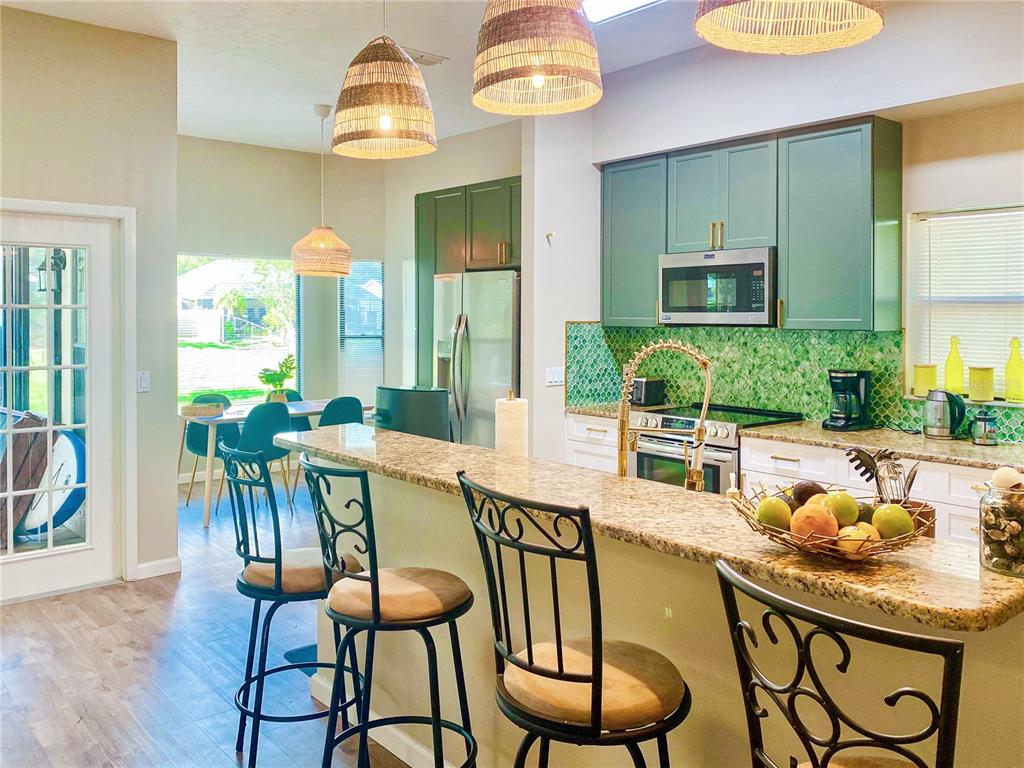A kitchen with green cabinets, granite countertops, a tiled backsplash, and a breakfast bar — 4907 82ND PLACE E, SARASOTA, FL