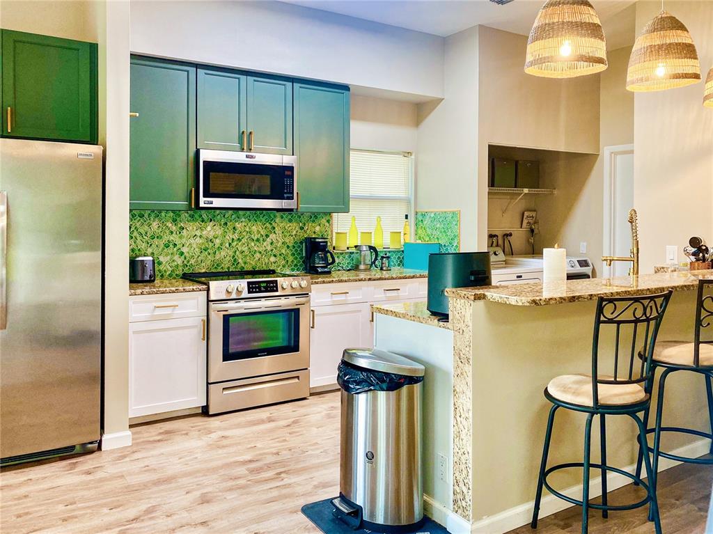 A kitchen features green upper cabinets, white lower cabinets, stainless steel appliances, and a breakfast bar — 4907 82ND PLACE E, SARASOTA, FL
