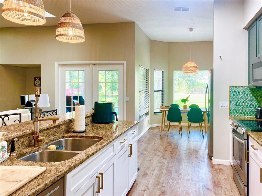 A kitchen with granite countertops, white cabinets, and a dining area with green chairs — 4907 82ND PLACE E, SARASOTA, FL