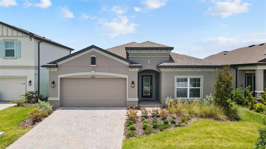 A single-story house with a gray stucco exterior, a paved driveway, and a two-car garage — 32034 SAPNA CHIME DRIVE, WESLEY CHAPEL, FL