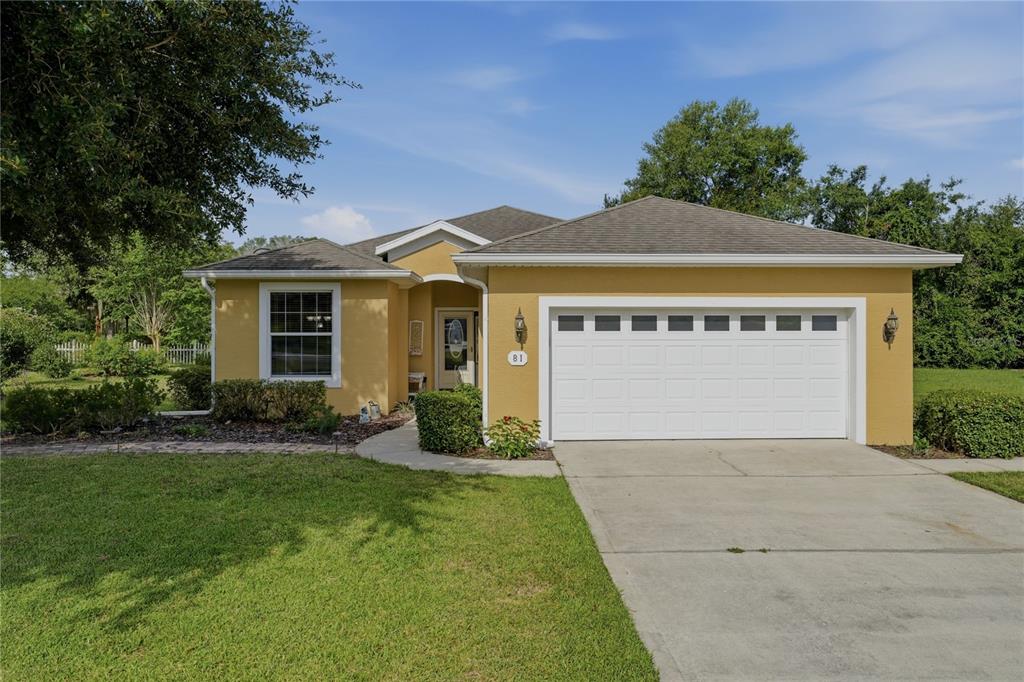 A single-story yellow house with a white garage door and a concrete driveway — 81 TWIN LAKE CIR, UMATILLA, FL