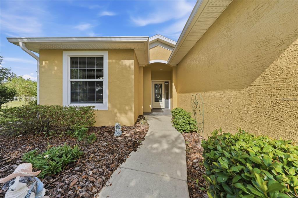 A yellow stucco house exterior features a concrete walkway leading to a recessed front entrance — 81 TWIN LAKE CIR, UMATILLA, FL
