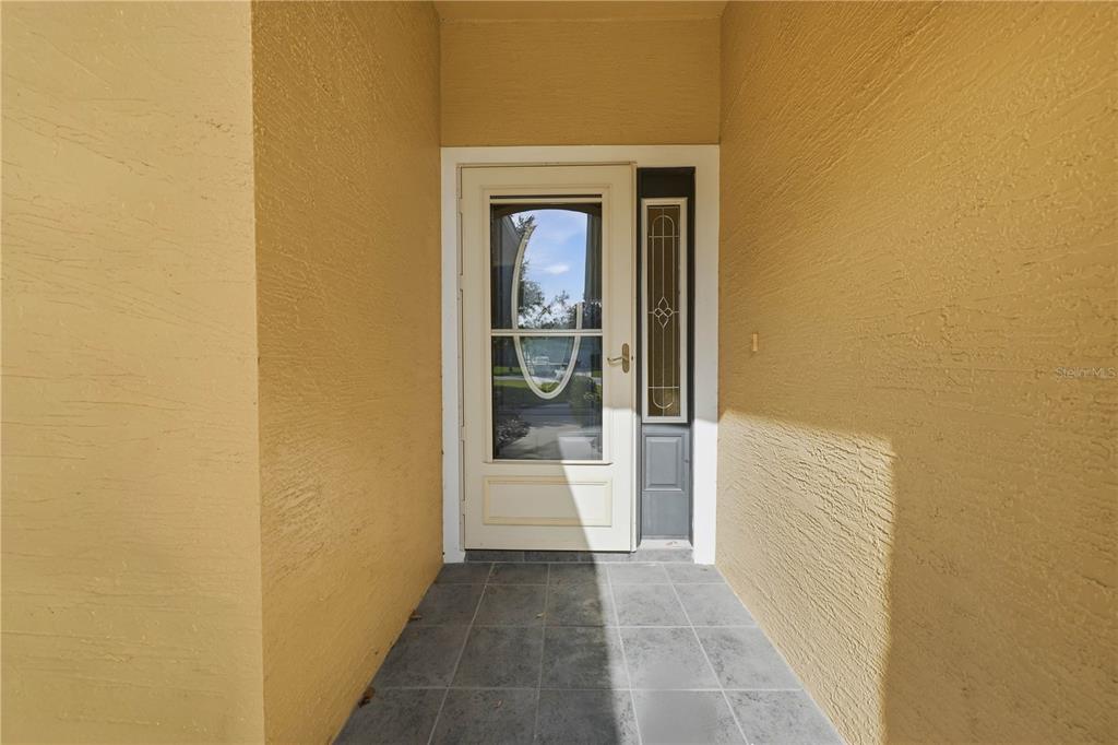 A covered entryway features a white front door with a glass insert and tiled flooring — 81 TWIN LAKE CIR, UMATILLA, FL