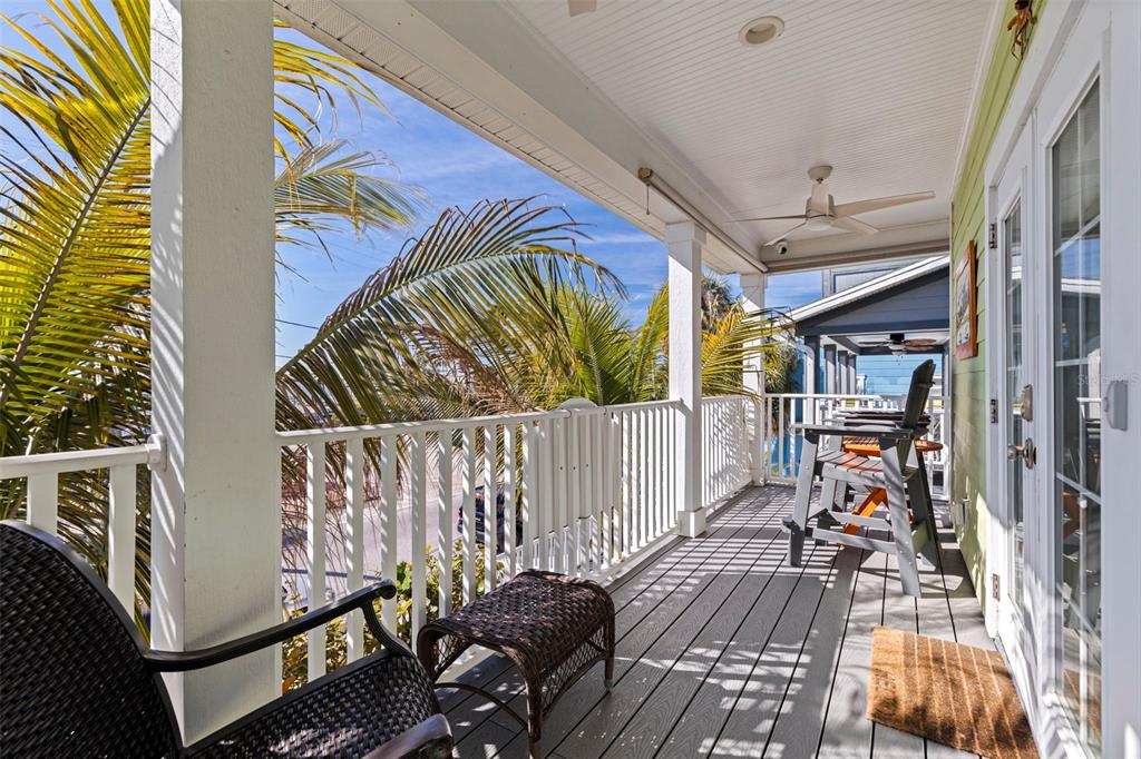 A covered wooden balcony features white railings, wicker furniture, and views of palm trees — 5429 ESSEX AVENUE S, GULFPORT, FL