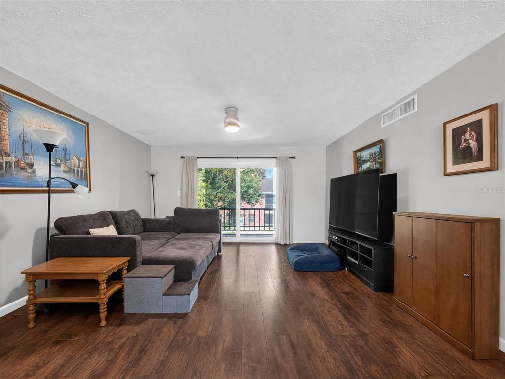 A living room features dark wood flooring, a sectional sofa, a television, and sliding glass doors — 4386 LAKE UNDERHILL ROAD UNIT D, ORLANDO, FL