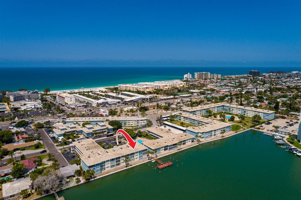 An aerial view shows a waterfront apartment complex with a red arrow pointing toward it — 6061 2ND STREET E UNIT 55, ST PETE BEACH, FL