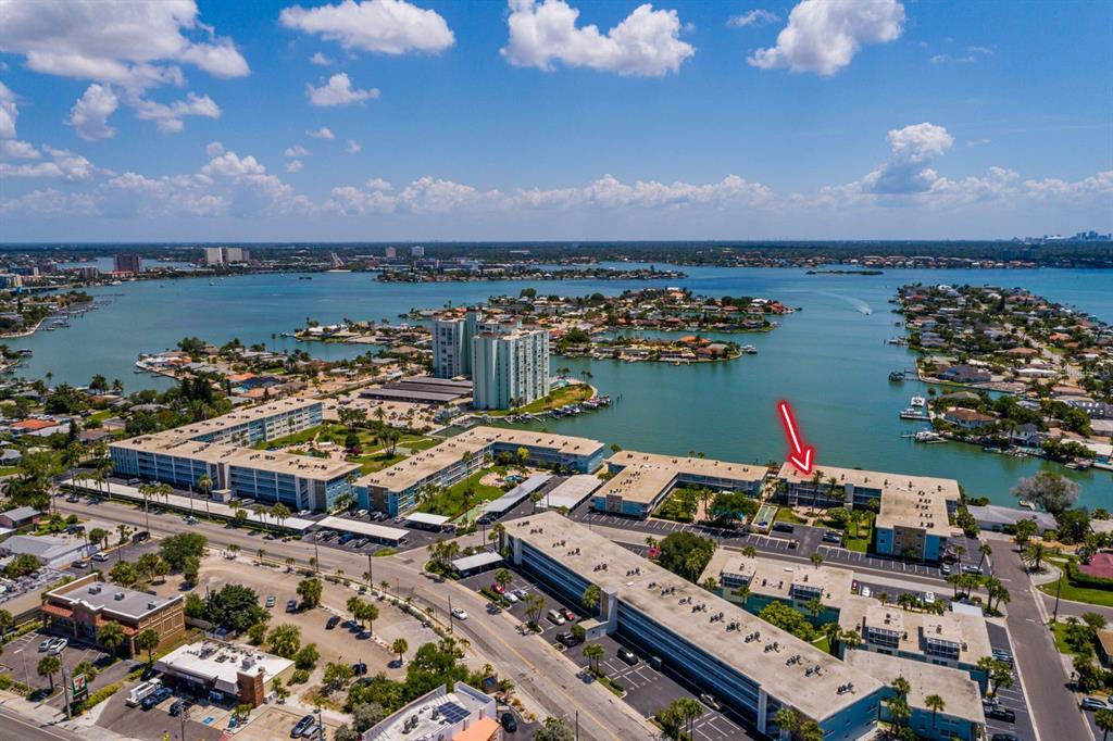 An aerial view shows a multi-story apartment complex near a bay with a red arrow — 6061 2ND STREET E UNIT 55, ST PETE BEACH, FL