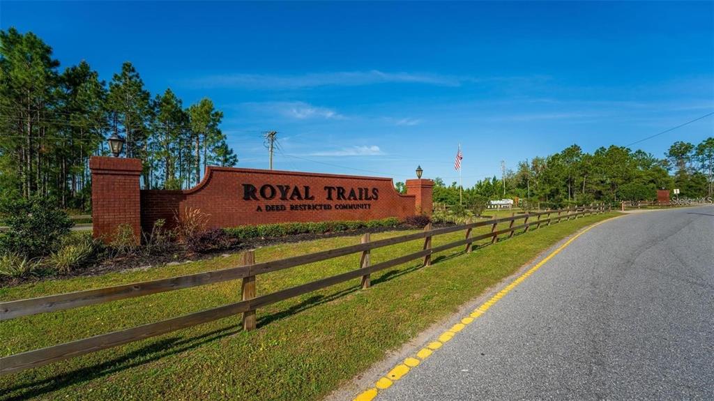 A brick sign for Royal Trails community stands beside a road with a wooden fence — APRICOT AVENUE, EUSTIS, FL