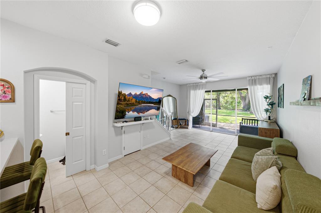 A living room features tile flooring, a wall-mounted television, a green sofa, and sliding glass doors — 2405 EARLSWOOD COURT, BRANDON, FL
