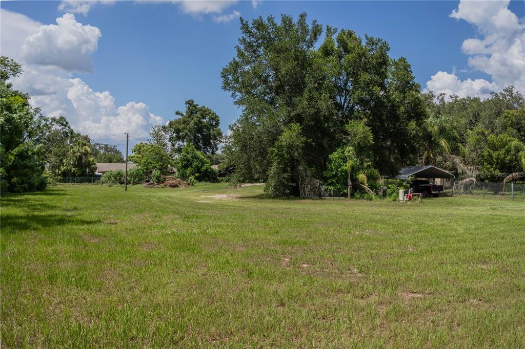 A large, grassy, vacant lot features mature trees and a small carport on the right — 441 OVERHILL DRIVE, BRANDON, FL