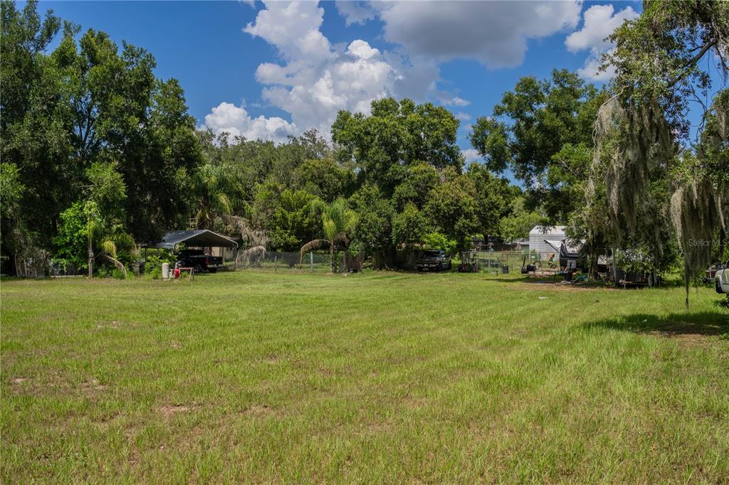 A large, grassy lot features several mature trees, a metal carport, and parked vehicles — 441 OVERHILL DRIVE, BRANDON, FL