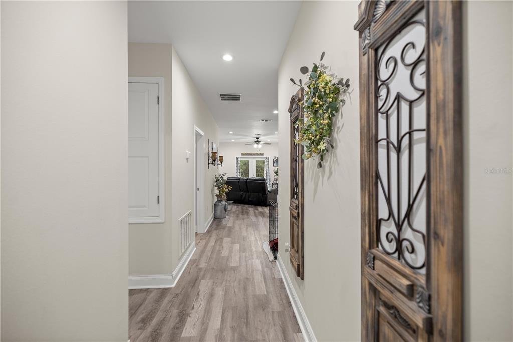 A hallway with light wood-look flooring leads to a living area with a ceiling fan — 2 MAGNOLIA PASS TRACE, OCKLAWAHA, FL