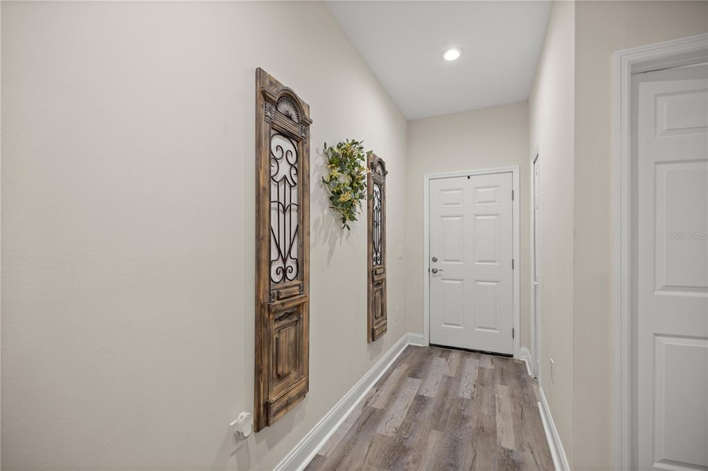 A hallway with light walls, wood-look flooring, and decorative wall panels near an entrance door — 2 MAGNOLIA PASS TRACE, OCKLAWAHA, FL