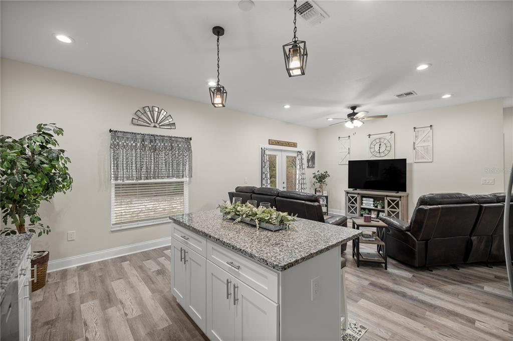 A kitchen island with granite countertops sits in front of a living room with dark furniture — 2 MAGNOLIA PASS TRACE, OCKLAWAHA, FL