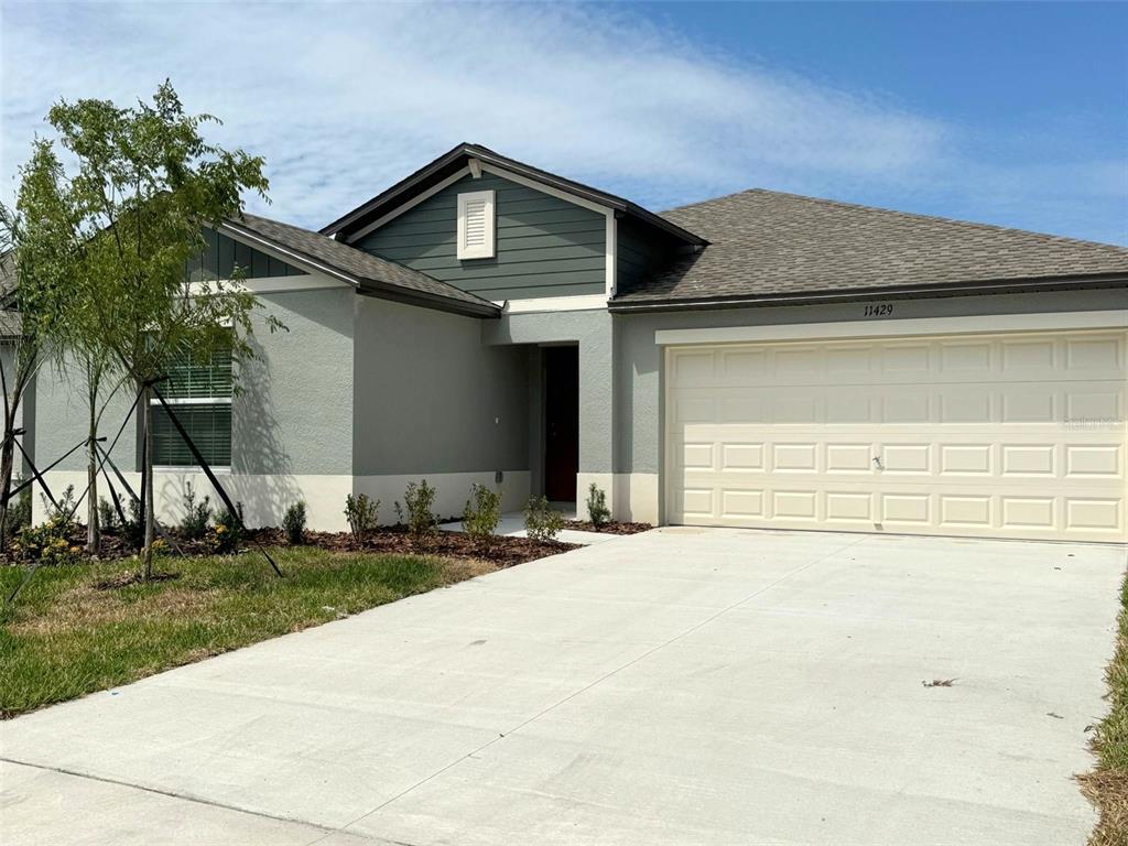 A single-story house with a two-car garage, gray stucco exterior, and green siding accents — 11429 LINDEN DEPOT ROAD, SAN ANTONIO, FL