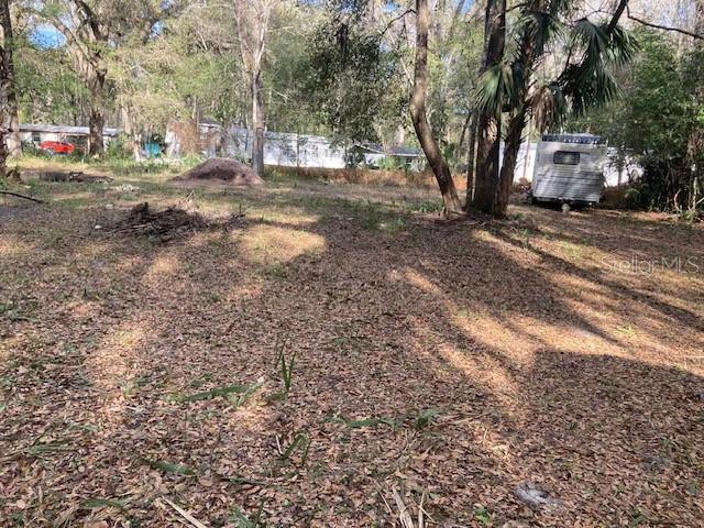 A wooded, leaf-covered lot features a small travel trailer parked among the trees — 2456 N JUNGLE CAMP ROAD UNIT 1, INVERNESS, FL