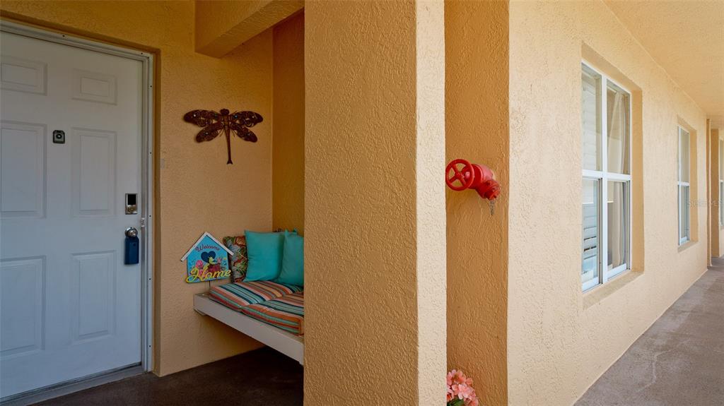 A covered entryway features a white door, a small bench with pillows, and a red valve — 4570 PINEBROOK CIRCLE UNIT 302, BRADENTON, FL