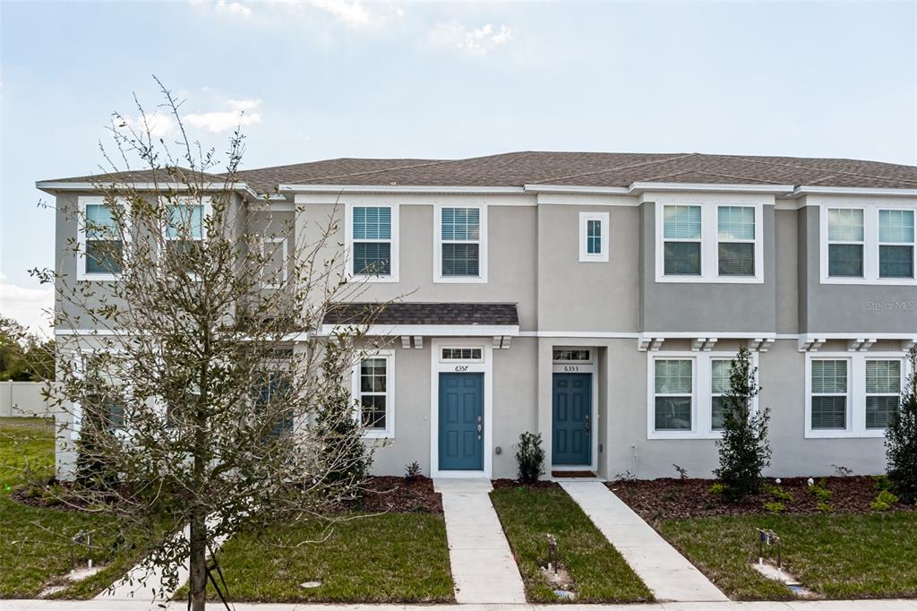 A two-story townhouse exterior with gray stucco walls, dark blue front doors, and shingled roofing — 6357 FAIRMONT LANE, PALMETTO, FL