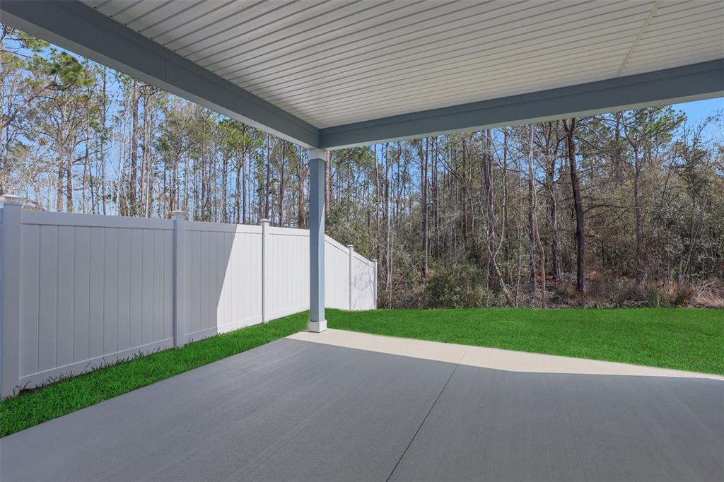 A covered concrete patio overlooks a grassy backyard enclosed by a white vinyl fence — 3550 BELSTEAD WAY, ORANGE PARK, FL