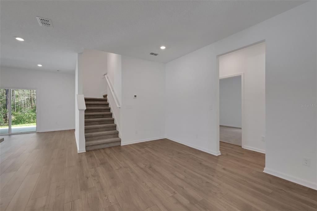 An interior view shows a room with wood-look flooring, carpeted stairs, and white walls — 3550 BELSTEAD WAY, ORANGE PARK, FL