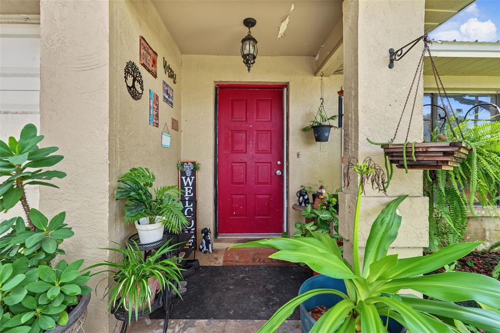 A red front door is centered on a covered porch decorated with various potted plants — 509 E DREW STREET, PLANT CITY, FL
