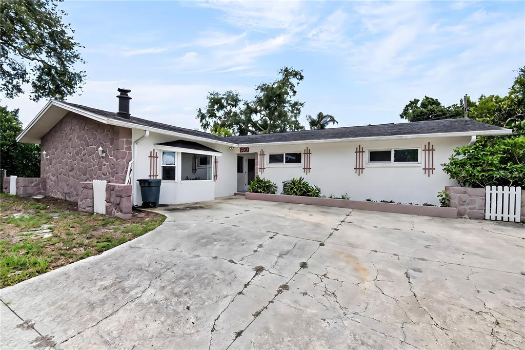 A single-story house with a stone-clad side wall, white stucco exterior, and a cracked concrete driveway — 1900 STANTON AVE, LARGO, FL