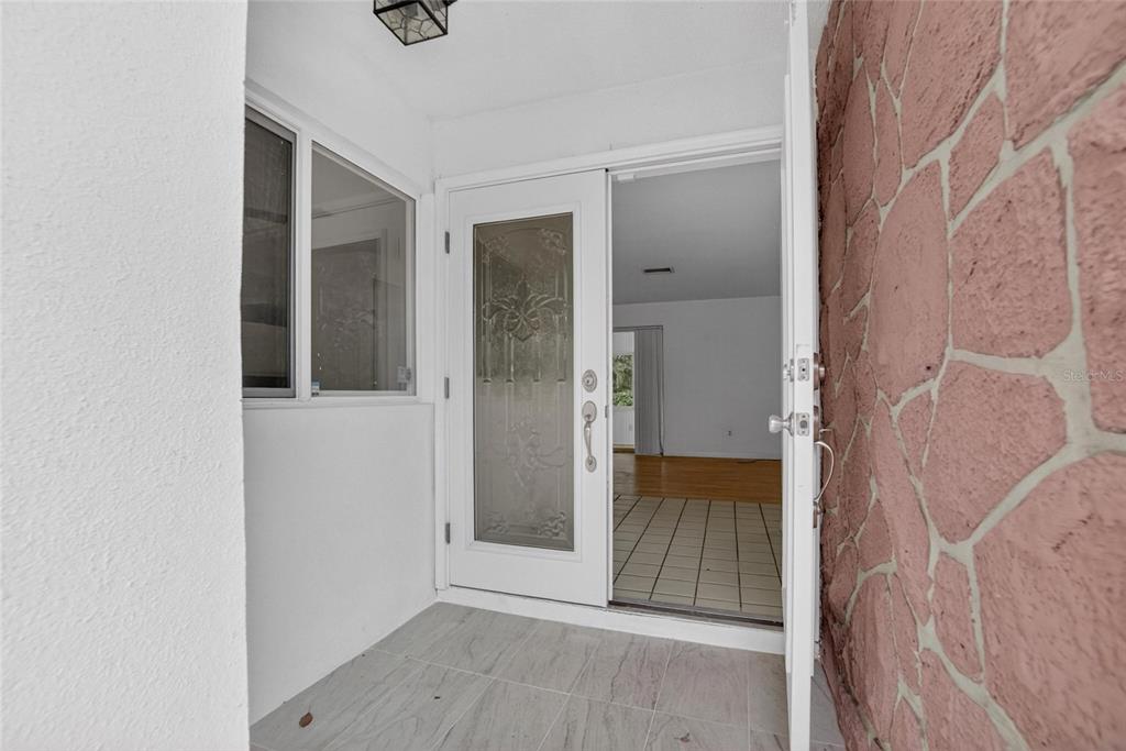 A front entryway features a glass-paneled door, tiled flooring, and a pink stone accent wall — 1900 STANTON AVE, LARGO, FL