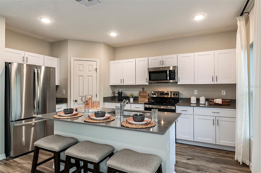 A kitchen features white cabinets, stainless steel appliances, a gray island, and three bar stools — 4337 RIVERBEND BOULEVARD, HAINES CITY, FL