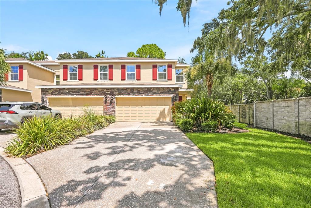 A two-story townhouse with a stone-accented facade, two garage doors, and a concrete driveway — 13105 CANOPY CREEK DRIVE, TAMPA, FL