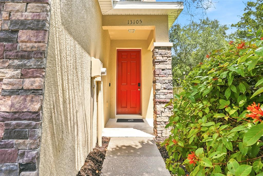 A red front door is framed by stone pillars and a concrete walkway — 13105 CANOPY CREEK DRIVE, TAMPA, FL