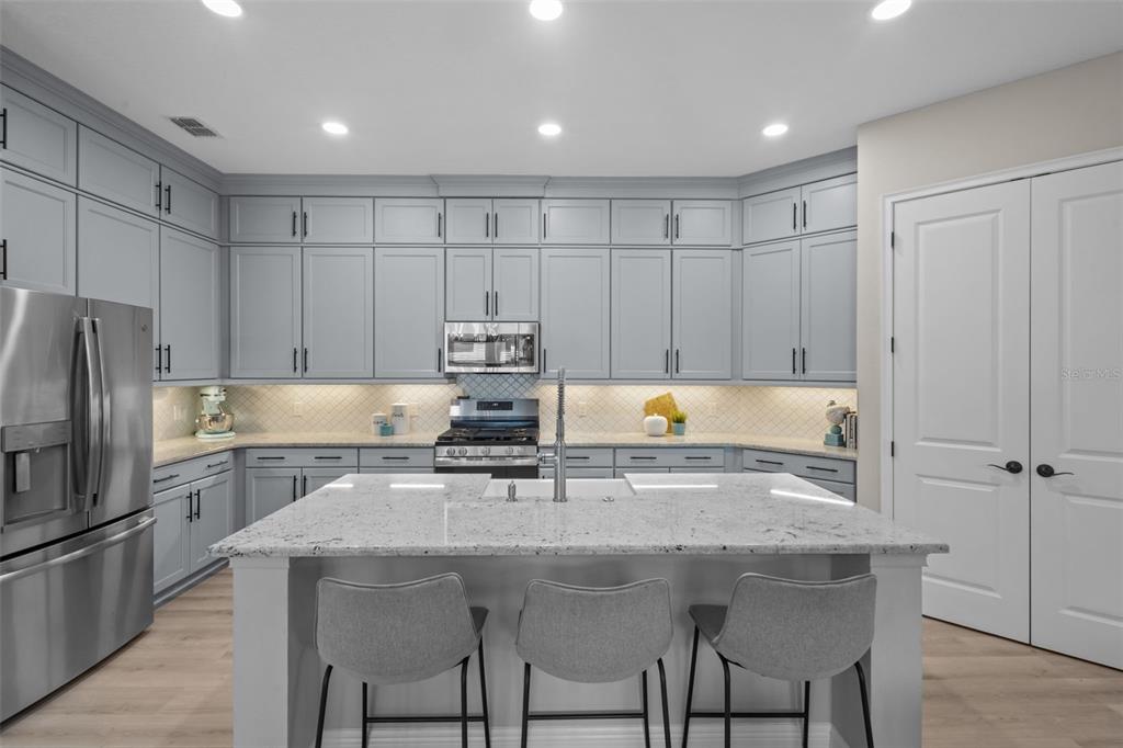 A modern kitchen features light gray cabinets, granite countertops, a central island, and stainless appliances — 15170 AVILES PARKWAY, ODESSA, FL