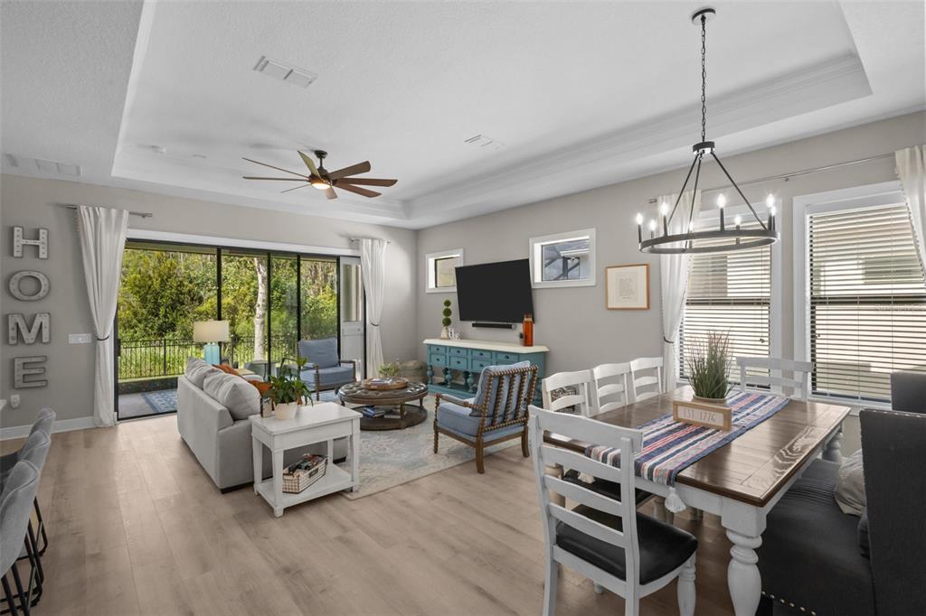 An open-concept living and dining area features light wood floors, a tray ceiling, and large windows — 15170 AVILES PARKWAY, ODESSA, FL