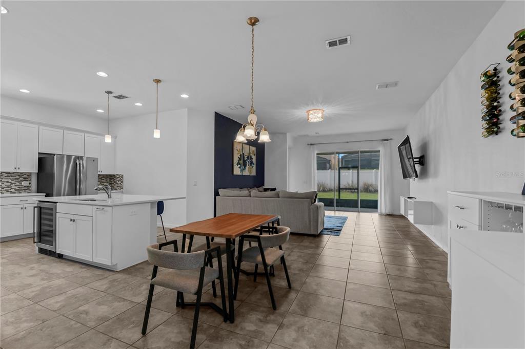 An open-concept kitchen and living area features white cabinetry, tile flooring, and a dining table — 9184 OLMO COURT, DAVENPORT, FL