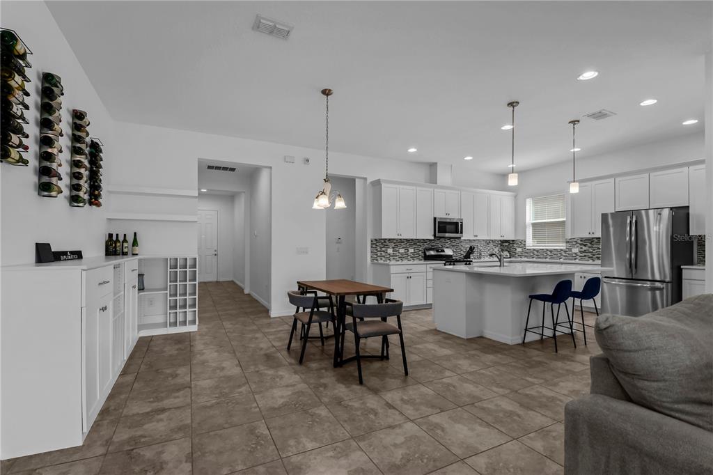 A modern kitchen features white cabinetry, a central island with bar seating, and wall-mounted wine racks — 9184 OLMO COURT, DAVENPORT, FL